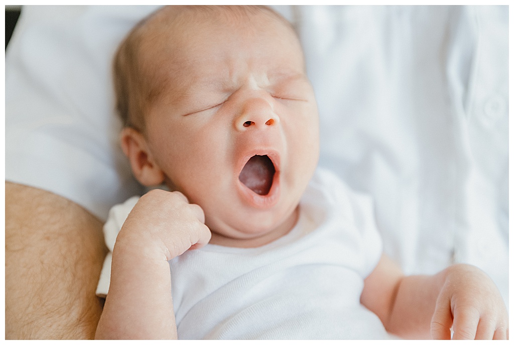 newborn baby yawning wearing white onesie