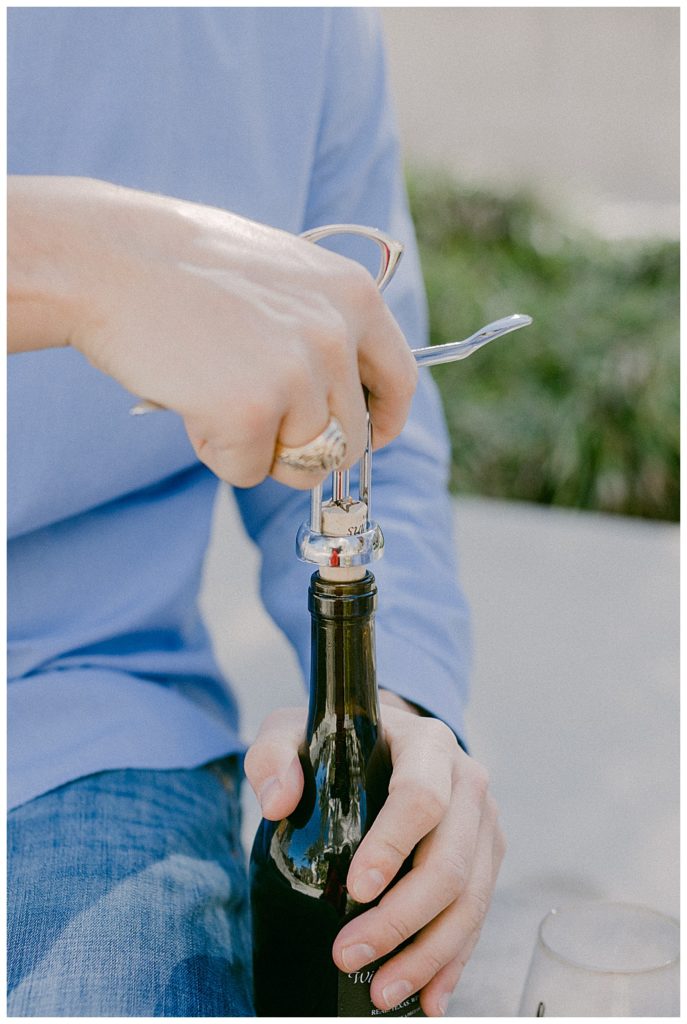 man using cork screw to open up bottle of wine