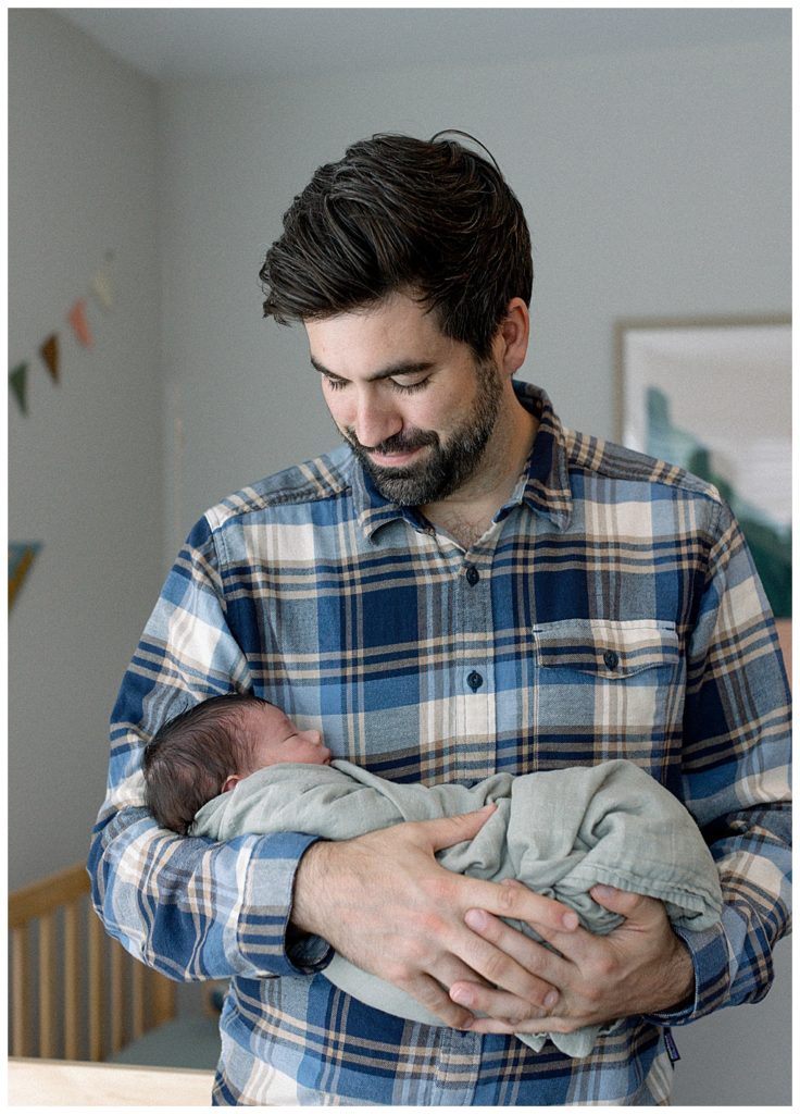 father cradling baby girl in sage blanket