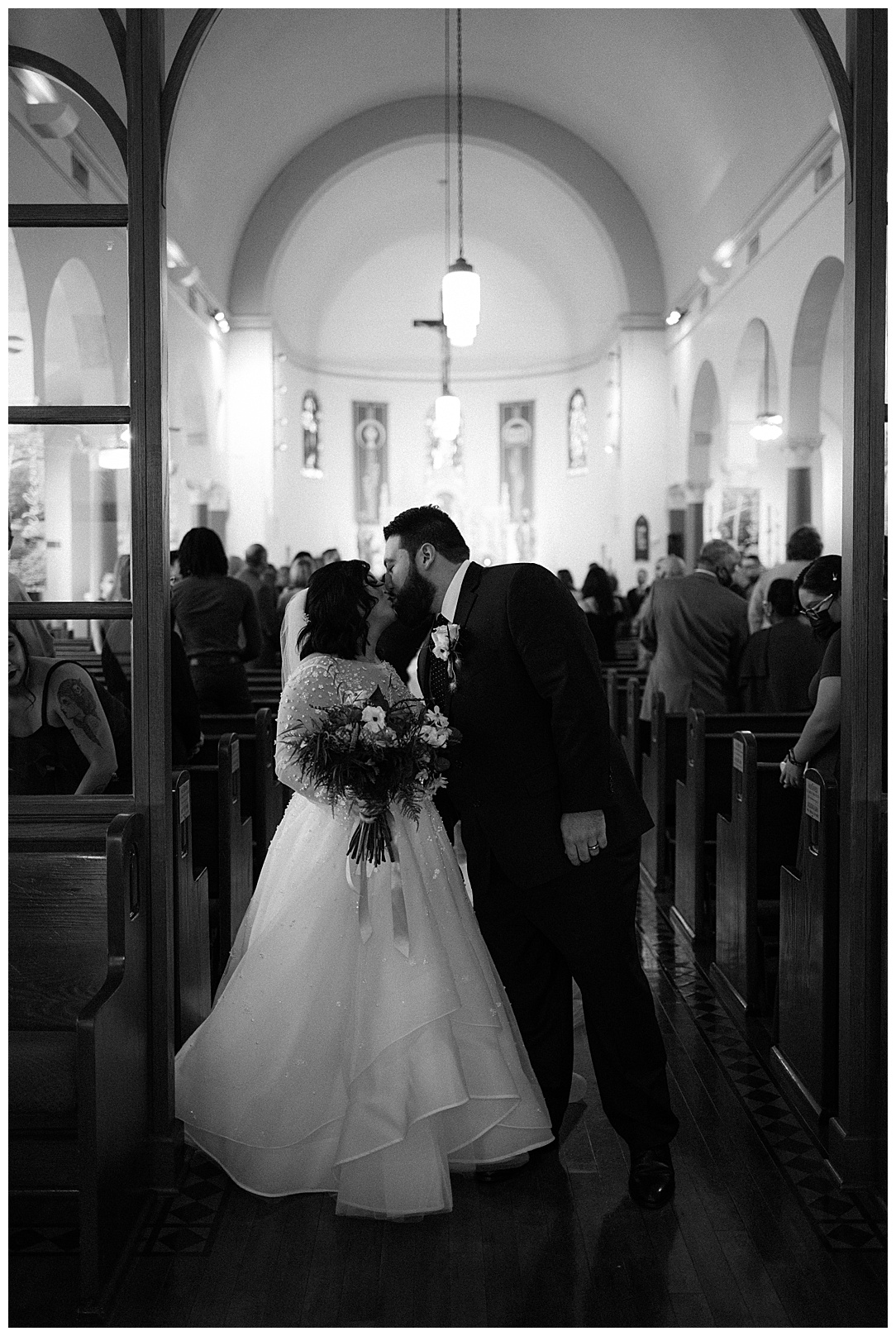 black and white picture of bride and groom kissing at the end of the aisle in church wedding