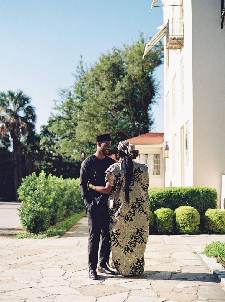 A couple stands together in traditional Nigerian dress at the Laguna Gloria for their Austin engagement photos.