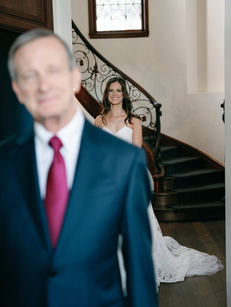 A bride stands behind her father for a first look built into her photography timeline for weddings.