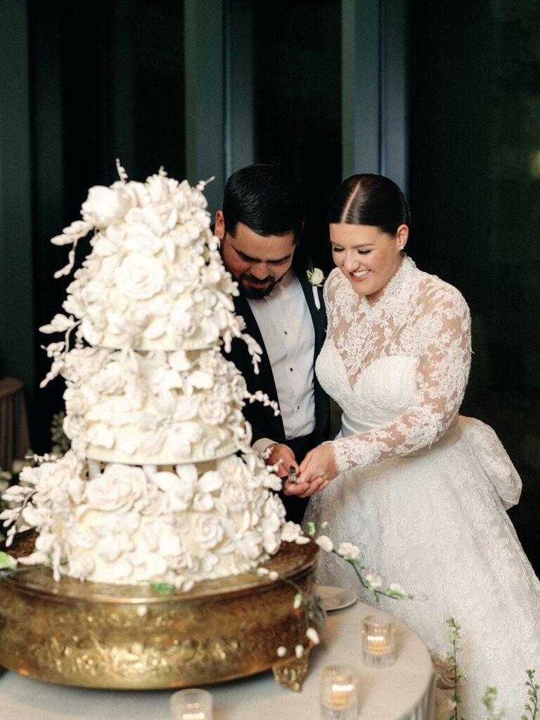 The bride and groom cut their cake together for the reception, a three tiered white cake covered in edible floral decor.