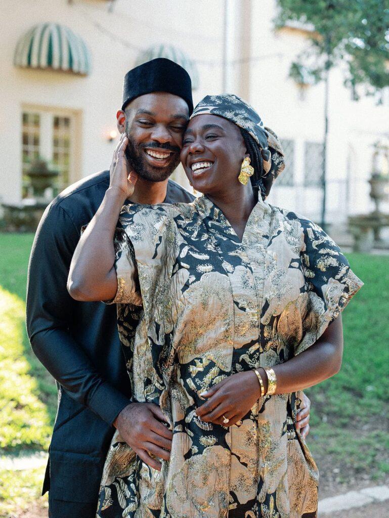 A man stands behind his new fiance on the grounds of a museum as they laugh together for their Austin engagement photos.