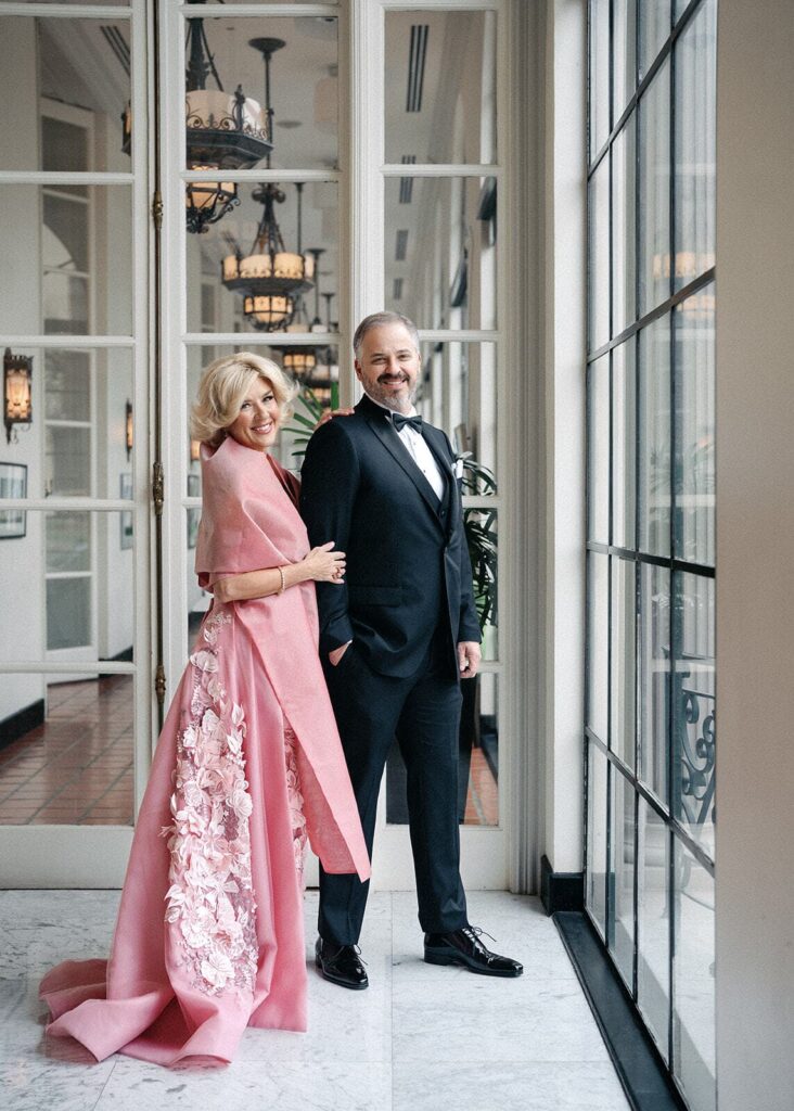 The mother and father of the bride pose together before the Witte Museum wedding, the mother of the bride wearing a pink, floor-length gown with white floral appliques.