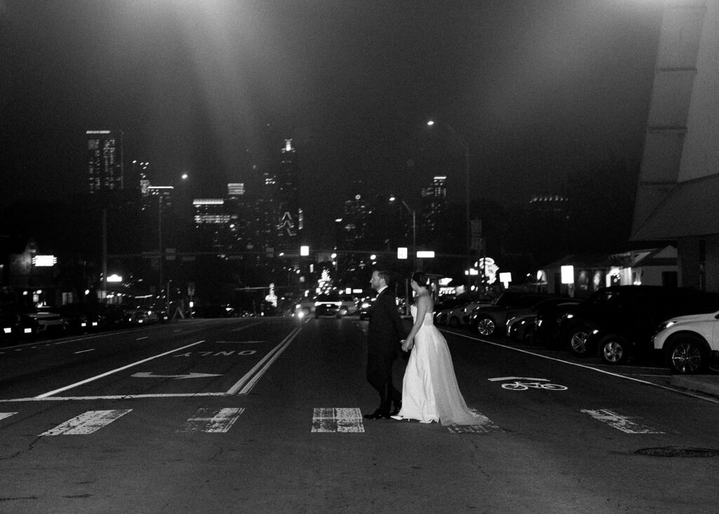 A couple walks across the street with the city behind them with a moment to themselves as built into their wedding photography timeline.
