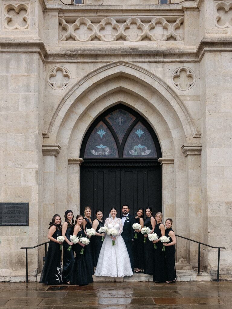 A bride poses with her bridesmaids in front of a cathedral.